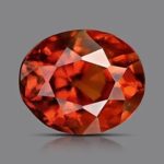 Oval-cut orange garnet gemstone with fiery internal reflections on a gray background.