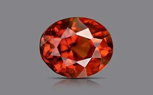 Oval-cut orange garnet gemstone with fiery internal reflections on a gray background.
